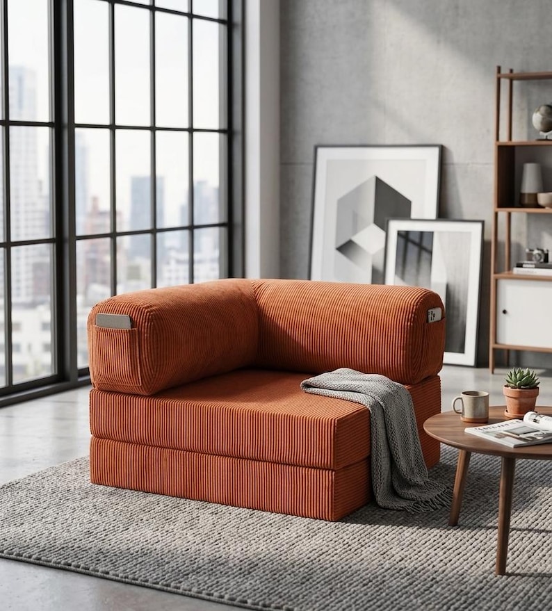 May include: A modular corner chair upholstered in burnt orange corduroy fabric. The chair features a low-profile design with a thick seat cushion, a backrest, and side armrests. A grey knit throw blanket is draped over the seat cushion.