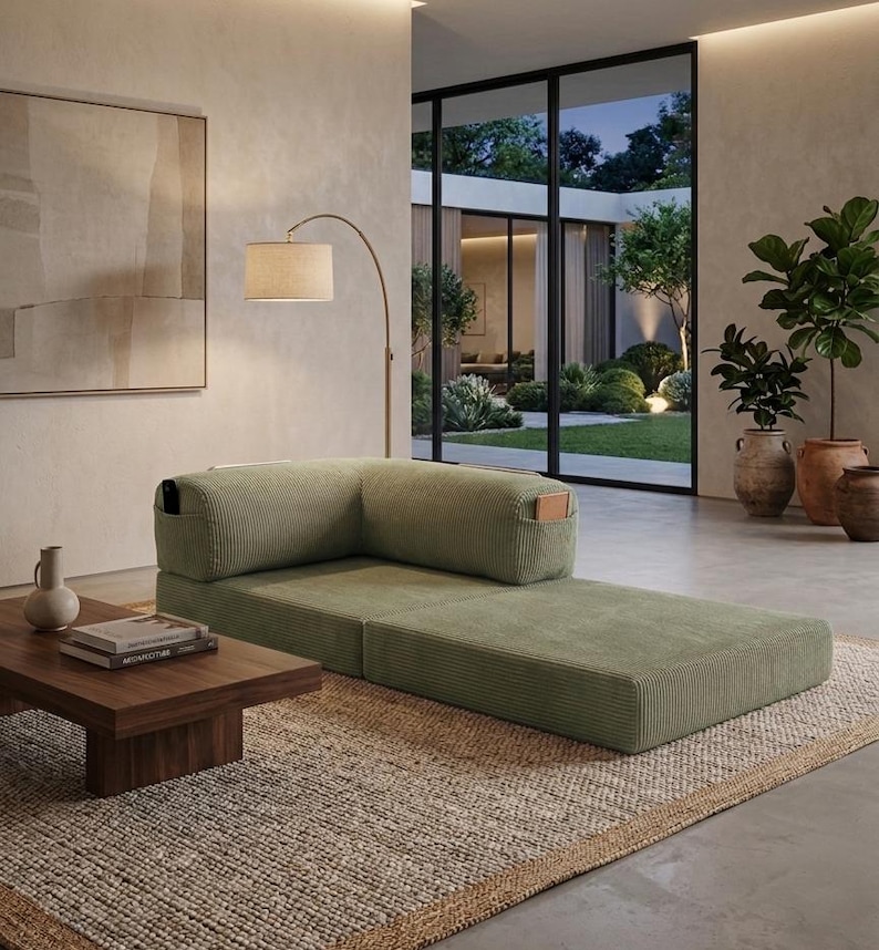May include: A low-profile, sage green corduroy floor sofa featuring an L-shaped backrest with integrated side pockets. The modular seating unit is upholstered in a textured ribbed fabric and sits directly on a woven area rug in a neutral tone.