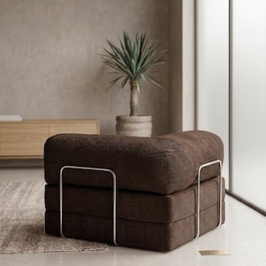 May include: A low-profile, square-shaped armchair upholstered in dark brown corduroy fabric. The seat features a thick, cushioned design supported by a sleek, silver-toned metal frame that wraps around the exterior sides of the base and backrest.