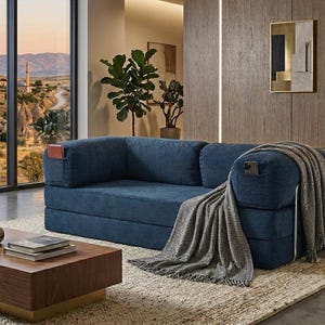 May include: A deep blue corduroy sofa featuring integrated side pockets on the armrests. The sofa is draped with a grey and white textured throw blanket. The design includes a low-profile backrest and seat cushions with a distinct ribbed fabric texture.