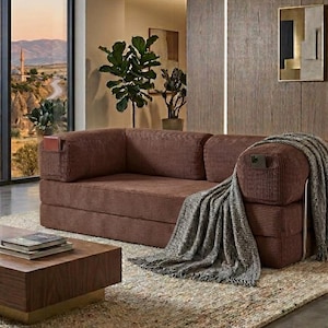 May include: A brown corduroy sofa with a low-profile design, featuring integrated side pockets on the armrests. A grey and white textured throw blanket with fringe edges is draped over the right arm, and the sofa has a structured, rectangular frame.