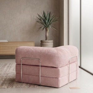 May include: A low-profile modular armchair upholstered in light pink corduroy fabric. The seat features a thick, square-shaped cushion design supported by a thin, silver-toned metal frame that wraps around the exterior sides of the base.