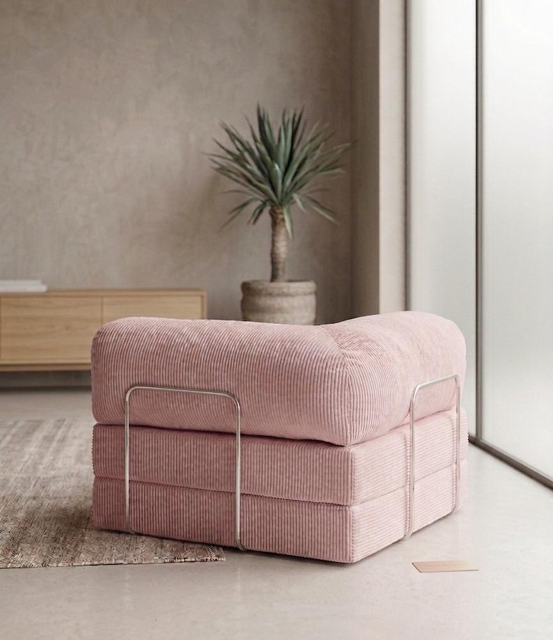 May include: A low-profile modular armchair upholstered in light pink corduroy fabric. The seat features a thick, square-shaped cushion design supported by a thin, silver-toned metal frame that wraps around the exterior sides of the base.