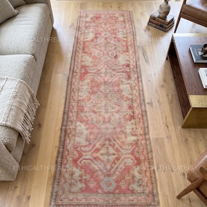 Peut inclure: Un tapis de couloir rectangulaire de style vintage avec un aspect vieilli. Le tapis présente un motif central dans des tons de rouge, crème et bleu clair, avec une bordure détaillée. Il est posé sur un parquet. Le tapis mesure environ 300 cm de long.