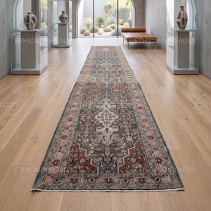Könnte beinhalten: Ein langer, rechteckiger Teppich mit einem aufwendigen, traditionellen Design. Der Teppich hat ein zentrales Medaillon und einen Rand in Braun-, Grau- und Rosatönen. Der Teppich liegt auf einem hellen Holzboden.