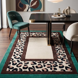 May include: A rectangular area rug featuring a central cream-colored rectangle bordered by a dark brown frame, surrounded by a wide band of leopard print in black, tan, and cream, finished with a solid teal green border on the outer edge.