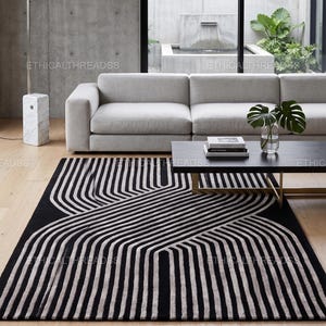 May include: A rectangular area rug featuring a black and off-white geometric pattern of intersecting, curved parallel lines. The rug is positioned on a light-colored wooden floor, with the text ETHICALTHREADSS overlaid across the image.