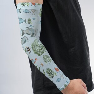 May include: A light blue arm sleeve featuring a repeating pattern of various marine life including fish, starfish, sea turtles, and green seaweed. The design is printed across the entire surface of the fabric, which covers the forearm and elbow.