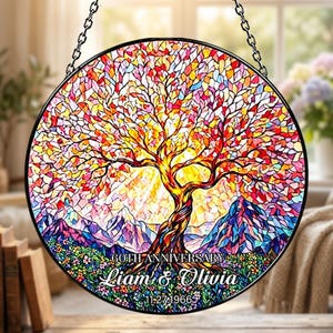 May include: A round stained glass panel featuring a colorful tree with a mountain backdrop. The tree has a brown trunk and branches with red, orange, and yellow leaves. The panel includes the text "60th Anniversary" and names "Liam & Olivia" with a date.