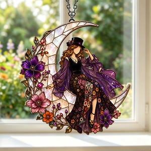 May include: A decorative hanging ornament featuring a crescent moon with a stained-glass effect. A figure wearing a black top hat and a flowing purple dress sits on the moon, which is adorned with purple, pink, and orange floral accents.