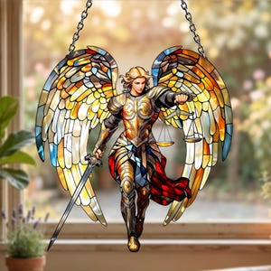 Peut inclure: Un attrape-soleil en vitrail représentant un ange aux grandes ailes multicolores dans des tons de jaune, orange et bleu. La figure porte une armure dorée, tient une épée argentée dans une main et équilibre une balance dans l'autre.