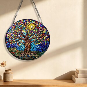 May include: A round stained glass panel featuring a colorful tree with a yellow sun. The tree has vibrant leaves in shades of red, orange, yellow, and green. The text "Liam & Olivia" and "11.27.1966" is displayed on the bottom. The panel is hanging from a chain.