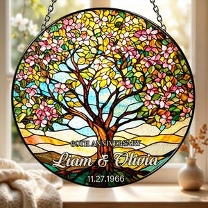 May include: A round stained glass panel featuring a tree with pink blossoms, yellow and green leaves, and a brown trunk. The text "60TH ANNIVERSARY" is above the names "Liam & Olivia" and the date "11.27.1966".