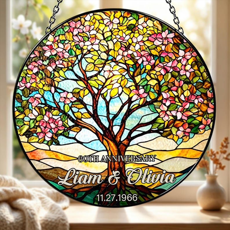 May include: A round stained glass panel featuring a tree with pink blossoms, yellow and green leaves, and a brown trunk. The text "60TH ANNIVERSARY" is above the names "Liam & Olivia" and the date "11.27.1966".
