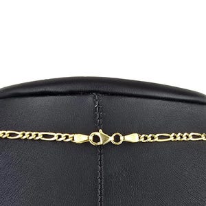K&ouml;nnte beinhalten: Eine goldfarbene Figaro-Kette mit einem Karabinerverschluss. Die Kette besteht aus einem sich wiederholenden Muster aus drei kleinen runden Gliedern, gefolgt von einem l&auml;nglichen ovalen Glied, die alle zu einem Strang verbunden sind.