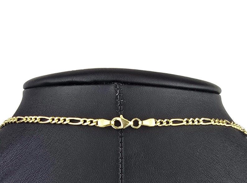 K&ouml;nnte beinhalten: Eine goldfarbene Figaro-Kette mit einem Karabinerverschluss. Die Kette besteht aus einem sich wiederholenden Muster aus drei kleinen runden Gliedern, gefolgt von einem l&auml;nglichen ovalen Glied, die alle zu einem Strang verbunden sind.