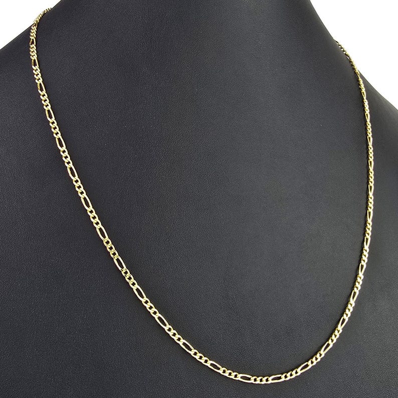 K&ouml;nnte beinhalten: Eine Figaro-Halskette aus Gelbgold mit einem sich wiederholenden Muster aus drei kleinen runden Gliedern, gefolgt von einem l&auml;nglichen ovalen Glied. Die Metallkette hat eine polierte Oberfl&auml;che und ist als durchgehende Schlaufe dargestellt.