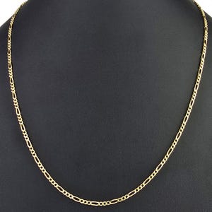 K&ouml;nnte beinhalten: Eine goldfarbene Metallkettenhalskette mit einem klassischen Figaro-Gliedermuster. Die Kette besteht aus einem sich wiederholenden Muster aus drei kleinen runden Gliedern, gefolgt von einem l&auml;nglichen ovalen Glied, das einen gleichm&auml;&szlig;igen Strang bildet.
