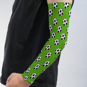 May include: An arm sleeve featuring a vibrant lime green background with a repeating pattern of black and white soccer balls. The sleeve extends from the upper arm to the wrist, providing full coverage with a fitted, flexible fabric construction.