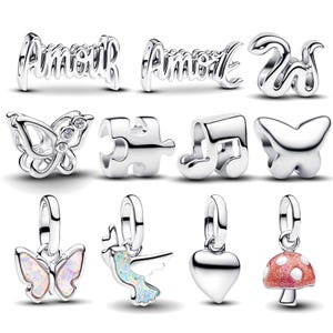 Puede incluir: Una colección de abalorios plateados, que incluyen la palabra "Amour", una serpiente, mariposas, una pieza de rompecabezas, una nota musical, un corazón, una seta y un pájaro. Algunos abalorios tienen detalles coloridos.
