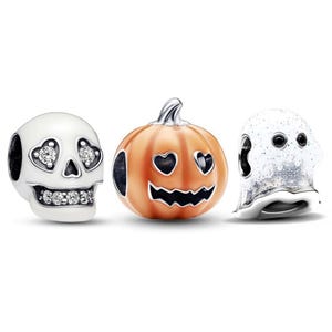Peut inclure: Trois breloques en métal pour bracelet, comprenant un crâne blanc avec des orbites en forme de cœur et des pierres claires, une citrouille orange avec des yeux en cœur et une bouche dentelée, et un fantôme blanc pailleté aux yeux ronds noirs.