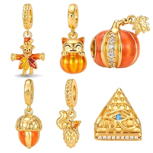 May include: A collection of six gold-toned metal charms featuring autumn and ancient themes. The set includes a scarecrow, a cat in a pumpkin, a pumpkin with clear stones, an acorn, a squirrel with a pinecone, and a pyramid with an Eye of Horus.
