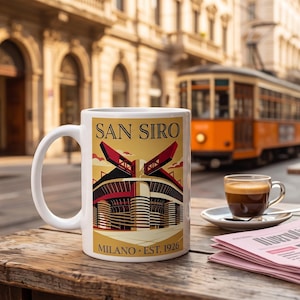 May include: A white ceramic mug featuring a graphic illustration of the San Siro stadium in Milan, with the text SAN SIRO and MILANO EST. 1926 printed on the front. The mug has a curved handle and a smooth finish, displaying a detailed architectural design.