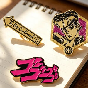Könnte beinhalten: Drei Emaille-Anstecknadeln auf einem Notizbuch. Eine ist ein goldener Pfeil mit dem Text "To Be Continued". Eine weitere ist eine goldene und rosa sechseckige Anstecknadel mit einer Charakterillustration. Die dritte ist eine japanische Textnadel in Pink und Schwarz.
