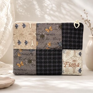Könnte beinhalten: Eine rechteckige Reißverschlusstasche mit einem Patchwork-Design aus sechs Quadraten. Die Stoffmuster umfassen Creme mit blauen Vögeln, Grau mit Schrifttext und gelben Schmetterlingen sowie dunkelblaues Karomuster. Der Name Fiona ist braun gestickt.