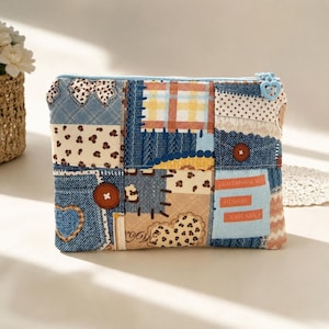 May include: A rectangular zippered pouch featuring a patchwork design of denim-textured fabric, brown leopard print, yellow plaid, and polka dots. The pouch includes a light blue zipper with a heart-shaped pull and text reading OPEN YOUR MIND TO THE POSSIBILITIES.