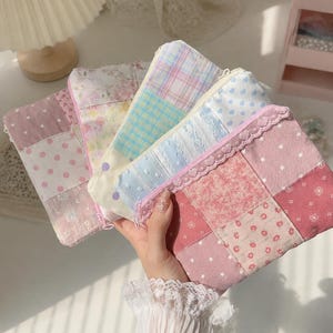 May include: A collection of four rectangular fabric pouches featuring patchwork designs in various pastel colours including pink, blue, yellow, and white. The pouches are decorated with patterns such as stars, polka dots, floral prints, and plaid, and each is finished with a zip closure and delicate lace trim.