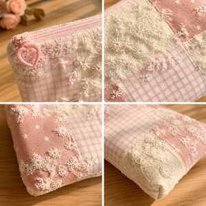 May include: A rectangular zipped pouch featuring a patchwork design of light pink gingham fabric, solid pink fabric with white stars, and cream-coloured floral lace overlays. The zip pull is a pink heart-shaped charm made of plastic.