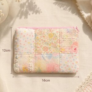 Puede incluir: Un estuche de tela rectangular con un dise&ntilde;o de patchwork de patrones florales y de corazones en tonos pastel rosa, amarillo y azul. El estuche tiene una cremallera rosa y mide 12 cm por 16 cm seg&uacute;n las marcas de medici&oacute;n visibles.