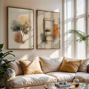 Könnte beinhalten: Zwei gerahmte Aquarelldrucke mit Bäumen und einem Torbogen in warmen Orange-, Braun- und Grüntönen. Sie hängen über einem cremefarbenen Ecksofa mit goldenen Kissen. Ein Glastisch und Topfpflanzen vervollständigen den Raum.