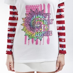 May include: A white t-shirt with long sleeves featuring a red and white horizontal striped pattern with navy blue anchors. The front displays a tie-dye sunflower graphic, a peace sign, and the text Don't Worry Be Hippie over a pink flag design.