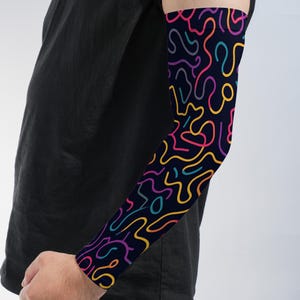 May include: An arm sleeve featuring a dark navy blue background with a continuous pattern of thin, winding lines in vibrant shades of yellow, magenta, purple, and teal. The sleeve covers the forearm and extends upward toward the upper arm area.