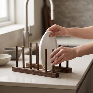 Può includere: Uno scolapiatti in legno marrone scuro caratterizzato da una serie di pioli verticali disposti in due file parallele su una base rettangolare, progettato per tenere i piatti in verticale. Realizzato in legno tinto con venature a vista.