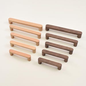 May include: A collection of ten wooden cabinet pulls arranged in two columns. The left column features five light-toned wood handles of varying lengths, while the right column displays five dark-toned wood handles, each with rounded edges.
