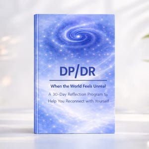 May include: A hardcover book titled "DP/DR" with a blue and white galaxy design on the cover. The text reads "When the World Feels Unreal" and "A 30-Day Reflection Program to Help You Reconnect with Yourself."