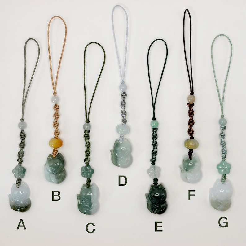 May include: A collection of seven jade fox pendants, each with a different colored cord and bead accents. The foxes are carved in various shades of green and white, with some featuring yellow or brown beads. The pendants are labeled A through G.