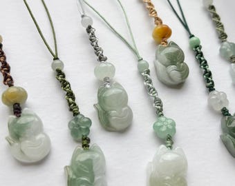 May include: A collection of jade fox pendants with various cord colors. Each pendant features a carved fox figure in shades of green and white, accented with beads and decorative knots. The pendants are designed for use as charms or accessories.