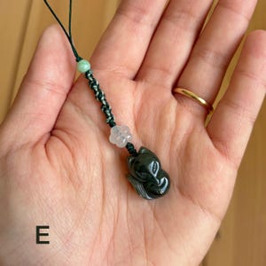 May include: A dark green jade fox pendant with a black and green braided cord, a light green bead, and a clear flower-shaped bead. The fox pendant is intricately carved and has a glossy finish. The cord is attached to a black string.