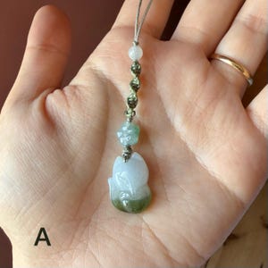 May include: A jade pendant in the shape of a fox, with a light green and white color gradient. The pendant is attached to a string with a flower and bead accent. The fox pendant is approximately 1.5 inches in height.