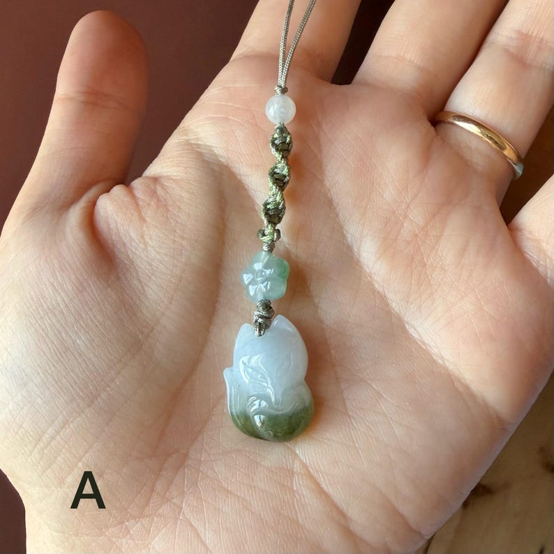 May include: A jade pendant in the shape of a fox, with a light green and white color gradient. The pendant is attached to a string with a flower and bead accent. The fox pendant is approximately 1.5 inches in height.