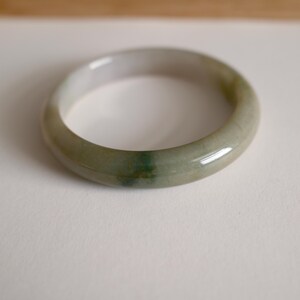 May include: A smooth, polished bangle bracelet crafted from translucent stone with a rounded profile. The material features a pale, milky white base color with subtle, mottled inclusions of soft green and grey throughout the circular band.