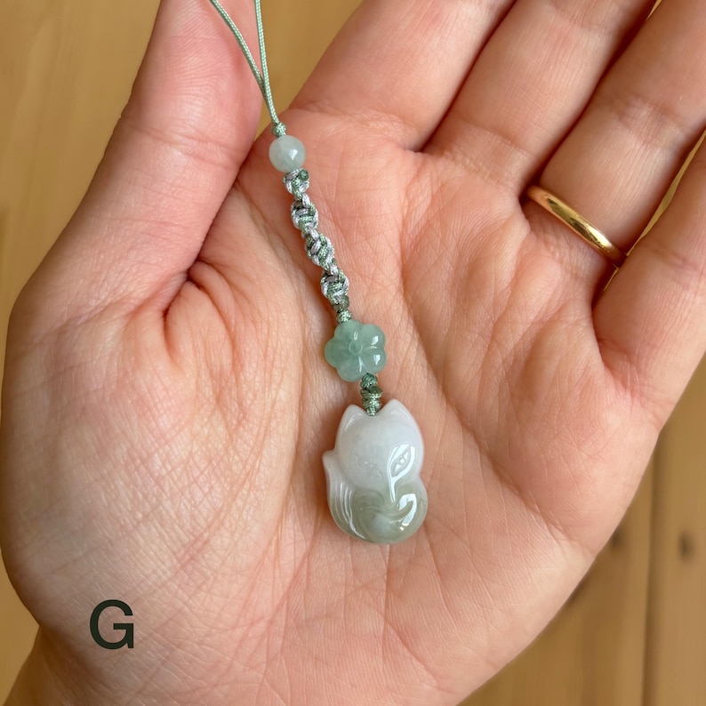 May include: A jade fox pendant with a light green cord. The fox is white and light green, with a flower and bead accent. The pendant is approximately 1.5 inches long.