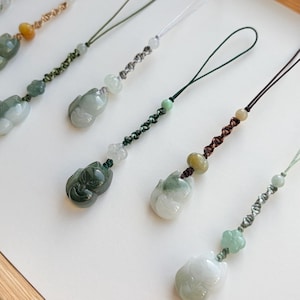 May include: Close-up of several jade fox charms with various cord colors. The charms are in shades of green and white, with intricate details. The cords are in green, brown, and white, with decorative beads. The charms are likely for a necklace or keychain.