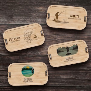Può includere: Quattro portapranzo rettangolari in bambù con chiusure in metallo. Ogni scatola presenta un design unico a tema pesca, con illustrazioni di pescatori, pesci e paesaggi. È incluso anche il testo "Moritz" e altre frasi.