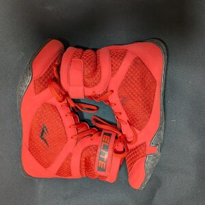 May include: Pair of red athletic shoes with black soles and laces. The shoes have a mesh design and the word "ELITE" is visible on the side. The shoes are designed for athletic activities.