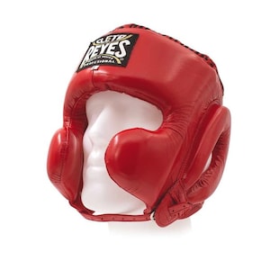 Peut inclure: Casque de boxe rouge avec protection des oreilles et des joues. Le casque est en cuir et porte le logo "REYES PROFESSIONAL". Conçu pour protéger la tête pendant la boxe ou le sparring.